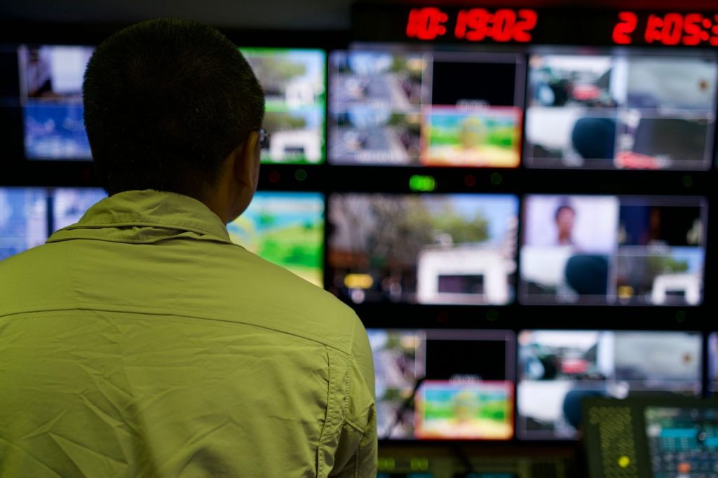 Homem observa vários monitores em uma sala de controle de televisão.