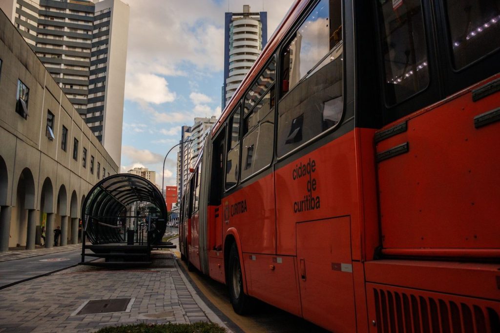 Ônibus vermelho parado em uma estação moderna no centro de Curitiba.