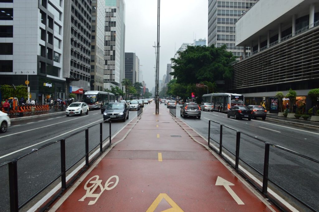 Avenida Paulista, em São Paulo, com ciclovia e veículos circulando em um dia nublado.
