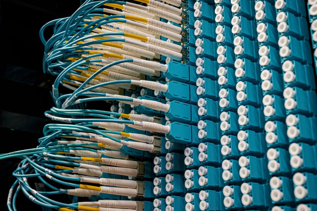 Petal: Meta projeta cabo submarino de capacidade petabit entre EUA e França Cabos de fibra óptica conectados a um painel azul em um data center.